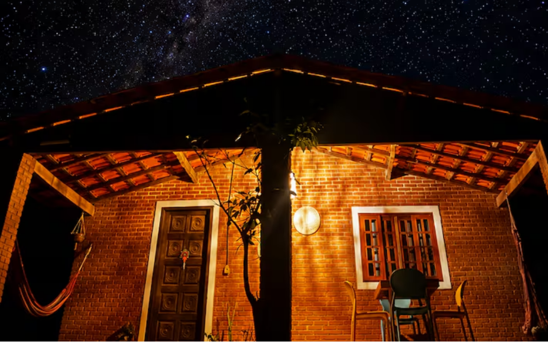 Fachada da Casa Afeto à noite iluminada sob um céu super estrelado em São Thomé das Letras